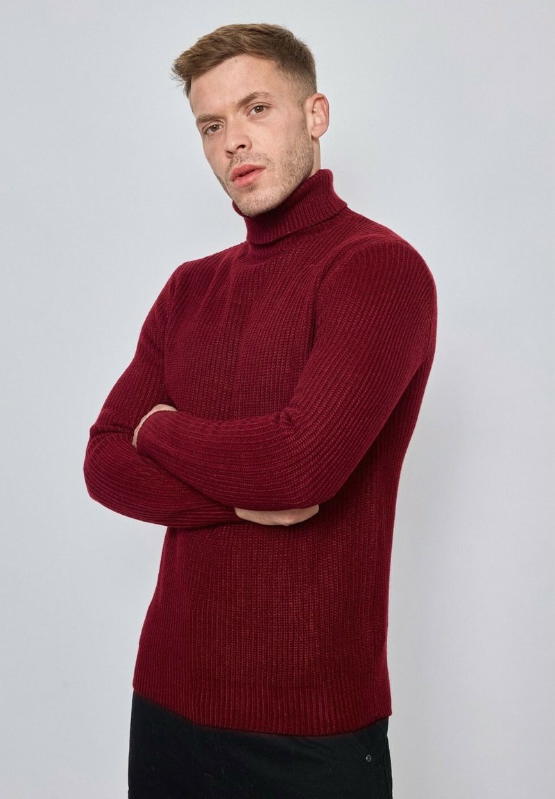 Pull col roulé côtelé bordeaux avec manches longues et silhouette ajustée, fabriqué en matière tricotée texturée, avec un col haut.