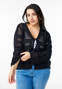 Svart stickad kofta med V-ringning, öppen fram och scalloped kant. Har en strukturerad, öppen vävdesign och dragsko-detalj.