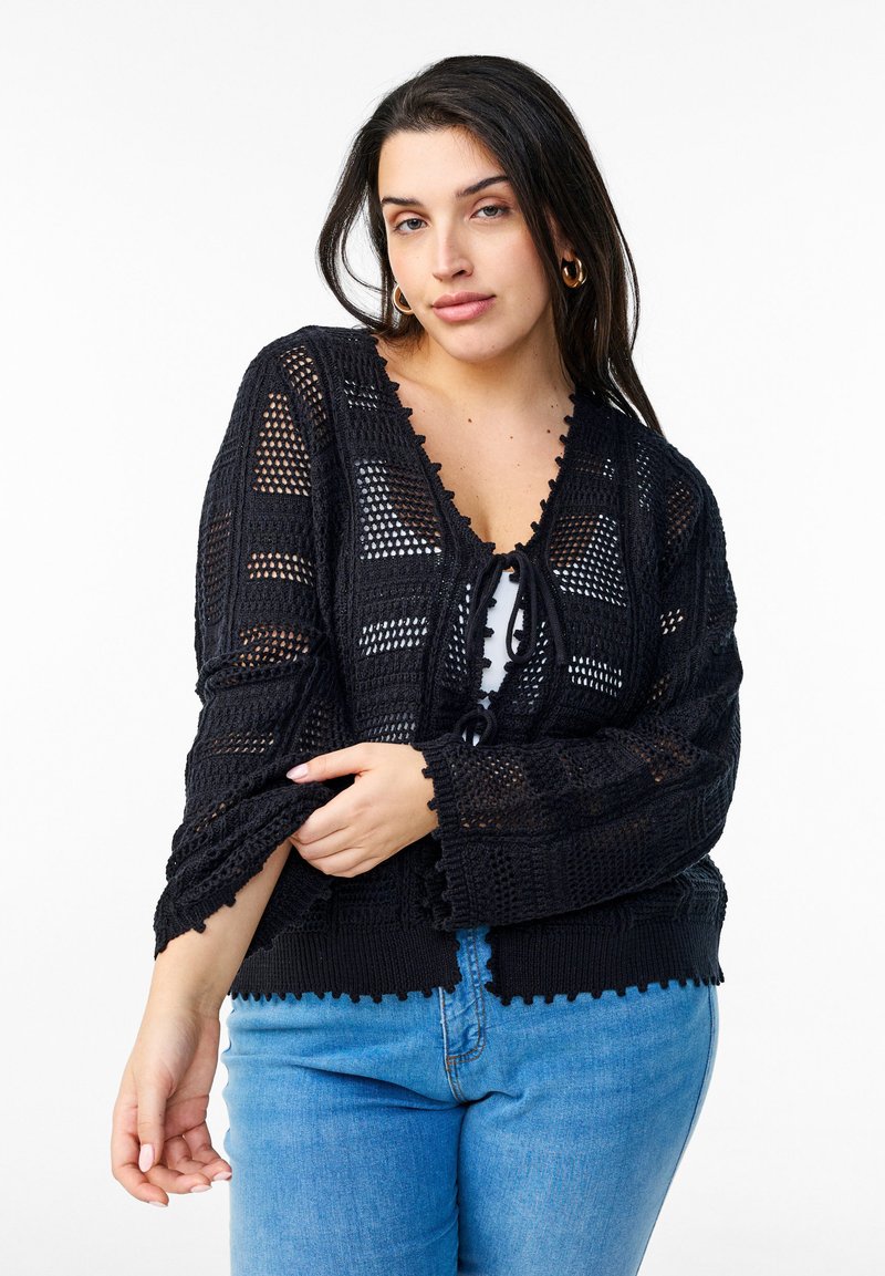 Svart stickad kofta med V-ringning, öppen fram och scalloped kant. Har en strukturerad, öppen vävdesign och dragsko-detalj.