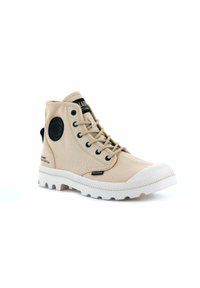 Zapatillas altas de lona beige con detalles en negro, punta redonda, diseño de cordones y suela de goma blanca con textura estampada y detalle de marca.