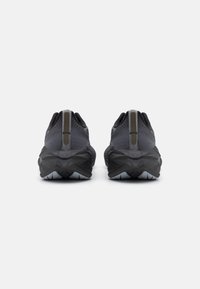 Chaussures de sport noires avec un dessus en tissu texturé, dotées d'une semelle en caoutchouc robuste avec des motifs géométriques et un accent réfléchissant au niveau du talon.