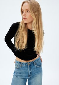 Top nero a maniche lunghe realizzato in materiale morbido, abbinato a jeans in denim chiaro con chiusura a bottone e design dritto.