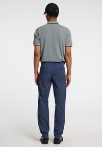 Grijze polo met korte mouwen en contrasterende kraagdetails, gecombineerd met marineblauwe broek. Het model staat zijwaarts, waardoor de pasvorm en stijl goed zichtbaar zijn.