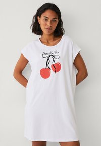 Hvid bomulds t-shirt kjole med korte ærmer. Har et grafisk print af to røde kirsebær bundet med en sort sløjfe og tekst ovenfor.