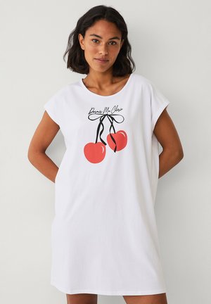 Witte katoenen t-shirt jurk met korte mouwen. Kenmerkt een grafische print van twee rode kersen vastgebonden met een zwarte strik en tekst erboven.