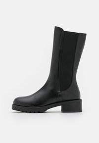 Botín negro hasta el tobillo con un cuerpo de cuero suave, paneles laterales elásticos, puntera redondeada y un tacón grueso con una suela de goma texturizada.