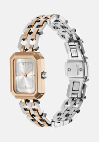 Obdľžnikové hodinky s dvojfarebným náramkom v ružovom zlate a nerezovej ocele. Majú strieborný ciferník s textúrovaným stredom a jednoduchými hodinovými údajmi.