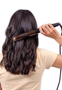 Fer à friser avec un design noir brillant et doré, doté d'un baril rond. L'utilisateur boucle des cheveux sombres et ondulés.