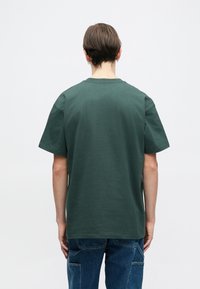 Tmavě zelené bavlněné tričko s uvolněným střihem, krátkými rukávy a klasickým kulatým výstřihem, z pohledu zezadu, s hladkým povrchem.