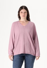 Ροζ πλεκτή ζακέτα με V-λαιμό, που διαθέτει λεπτομέρειες από καλσόν και μακριά μανίκια, συνδυασμένη με μπλε τζιν παντελόνι. Μαλακό, υφασμάτινο υλικό.