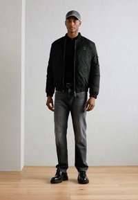 Svart bomberjakke, grå T-skjorte, grå denimjeans, svarte støvler og grå caps. Glatt materiale med ribbede mansjetter og midjebånd.