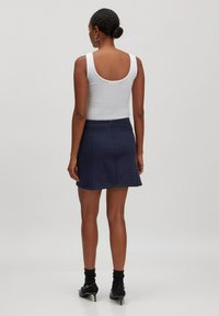 Marineblauwe A-lijn rok met een gladde textuur, voorzien van een achterrits en naden. Gepaard met een witte tanktop en zwarte hakken.