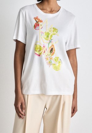 White short-sleeve shirt with colorful fruit and floral print worn with beige pants on a person against a plain background.