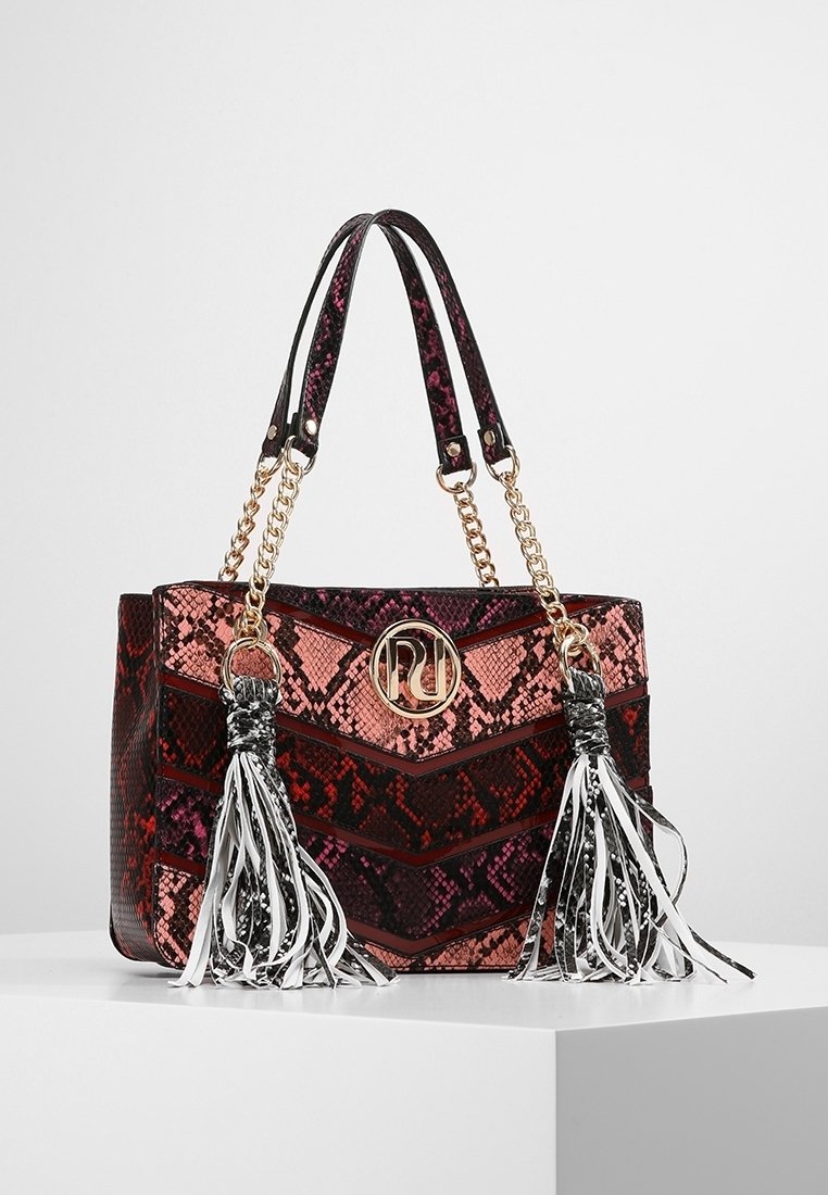 Sac cabas imprimé serpent rouge et noir avec ferrures dorées, anses chaîne pour l'épaule, et deux longs pompons noirs et blancs de chaque côté.