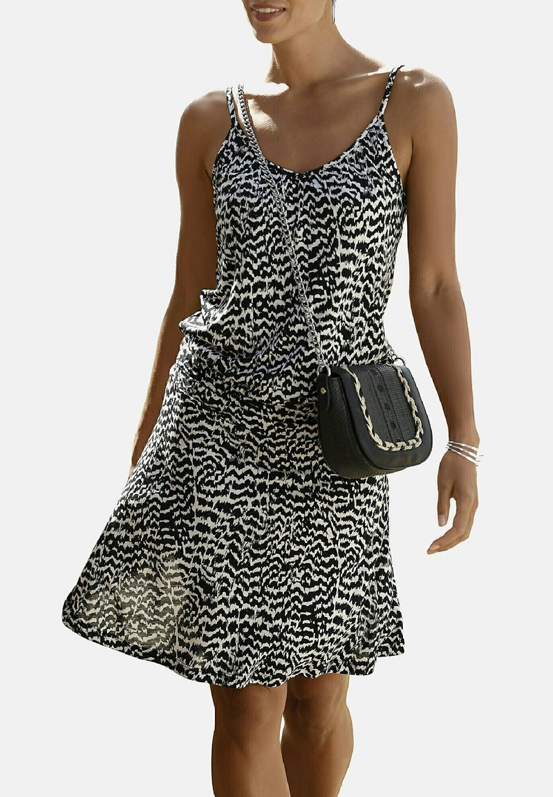 Svart och vit mönstrad solklänning med justerbara spännen, utsvängd fåll, kombinerad med en svart texturerad axelväska med flätad detalj.