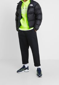 Svart puffjacka, neongrön hoodie, svarta byxor och marinblå sneakers med gröna accenter. Inkluderar vita strumpor och uppvikta byxben.