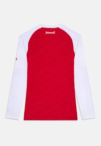 Rød og hvit langermet skjorte med et teksturert rødt design og Arsenal-logo over halsen, samt en hvit erme med en liten logoakcent.