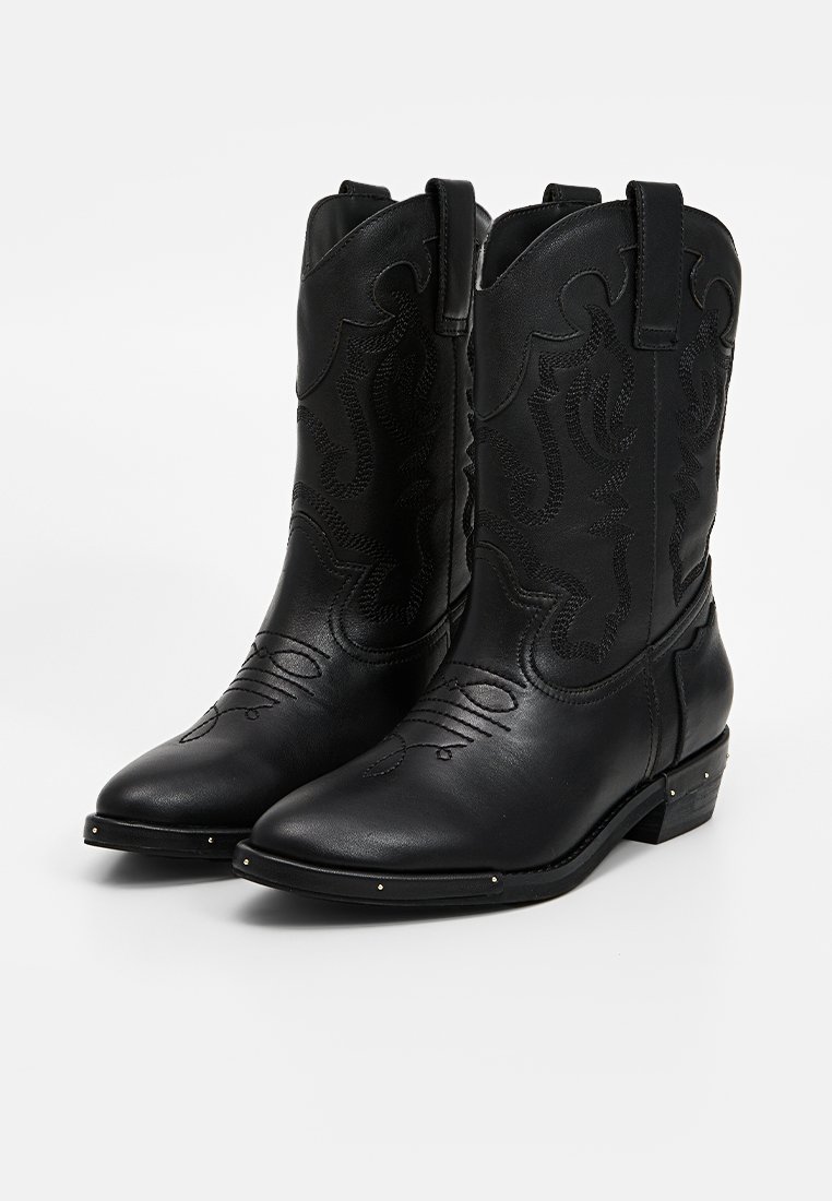 Botas de vaquero de cuero negro con punta afilada, patrones decorativos estampados, tiradores laterales y pequeños clavos metálicos en la suela.