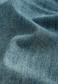 Taflă de denim într-o nuanță medie de albastru, cu o textură moale, având un model de țesătură twill și variații subtile de culoare.