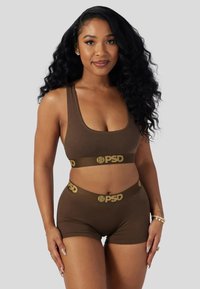 Brunt sports-bh- og shortssett med sømløst design, med et gullfarget logobånd. Stoffet virker mykt og elastisk.