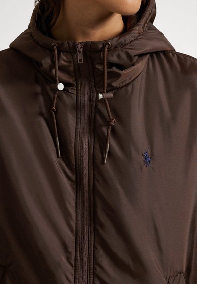 Καφέ μπουφάν με φερμουάρ και ομαλή υφή, ρυθμιζόμενη κουκούλα και κορδόνια. Διαθέτει μικρό μπλε λογότυπο στην αριστερή πλευρά του στήθους.