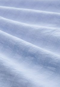 Hellblauer Stoff mit glatter Textur, der dezente gewebte Streifen in einer leicht dunkleren Schattierung aufweist und somit ein sanftes, schichtartiges Erscheinungsbild erzeugt.