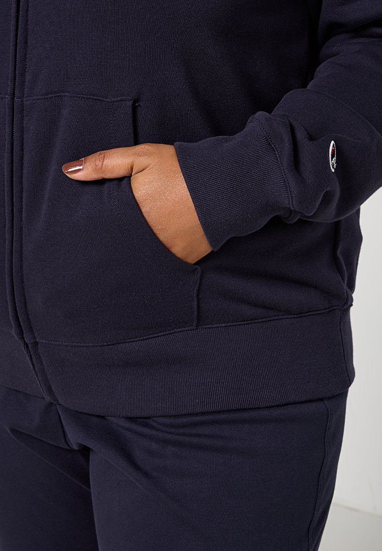 Felpa blu navy con zip realizzata in tessuto morbido. Presenta una tasca frontale e polsini a costine. Accentuata da un piccolo logo sulla manica.