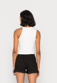 Camisola branca de alças canelada com um design de costas nadador, emparelhada com calções de ganga pretos com bainha virada e bolsos traseiros.