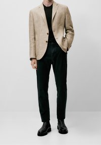 Beżowa lniana marynarka na dwa guziki z przednimi kieszeniami, zestawiona z czarnymi jeansami i czarnymi botkami. Prosty design, minimalne detale.