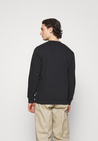 Sweatshirt negru cu guler rotund din material fleece, cu manșete și tiv ribbed. Purtați cu pantaloni bej, evidențiind un design simplu, fără modele.