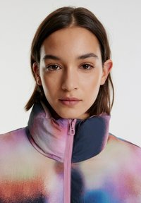 Multikleurige jas met hoge kraag, gemaakt van lichtgewicht materiaal. Voorzien van een roze rits en een kleurverloop in blauw, roze en oranje tinten.