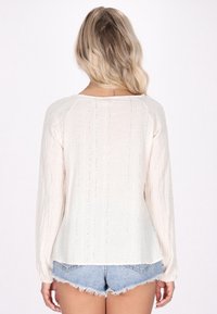 Lys beige langærmet skjorte med teksturerede lodrette striber og subtil glans. Har en afslappet pasform og afrundet kant. Sammen med denimshorts.