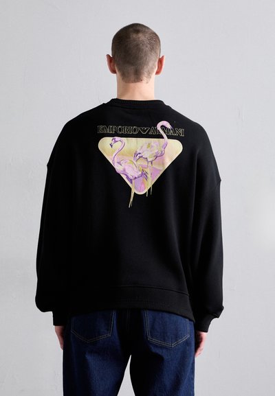 Sort sweatshirt med et stort pink og gult flamingo-grafik på en trekantet gylden baggrund, med "Emporio Armani" tekst ovenfor.