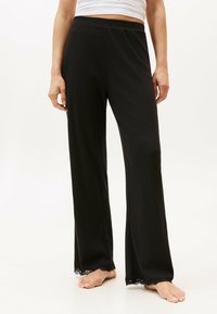 Zwarte ribbroek met een wijdbenig ontwerp en kanten trim aan de onderkant. Heeft een elastische tailleband voor comfort.