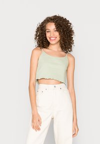 Top cropped em verde claro com nervuras e bainha em forma de onda, usado com jeans de cor creme de cintura alta. Textura suave, alças finas em espaguete.