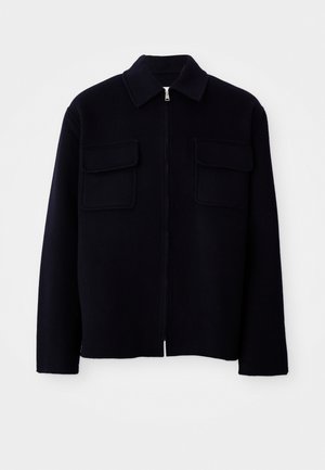 Zwarte wollen zip-up jas met een puntige kraag en twee borstzakken met flap, weergegeven op een witte achtergrond.