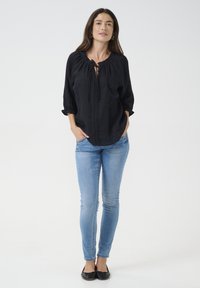 Blusa in lino nera con scollatura rotonda, dettaglio con coulisse e ricamo lungo la parte frontale; abbinata a jeans skinny blu chiaro e ballerine nere.