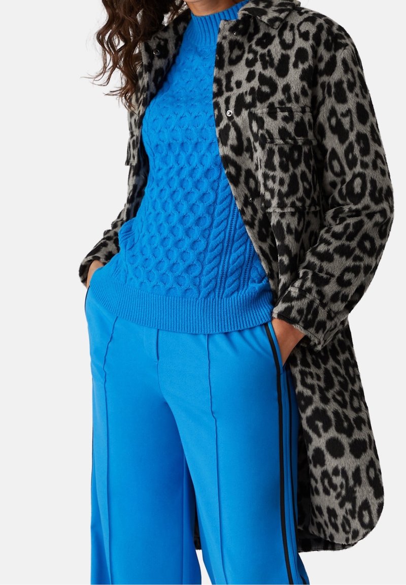 Leopardmönstrad kappa, texturerad blå kabelstickad tröja och klara blå vida byxor med svarta sidostriper. Tight och lagerdesign.