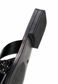 Semelle de sandale noire avec grip texturé, sangle en cuir tressé et talon lisse vue de profil sur fond blanc.