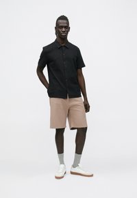 Zwart gestreept overhemd met korte mouwen en knoopsluiting, gecombineerd met beige shorts, grijze sokken en witte sneakers. Simpel ontwerp en casual pasvorm.