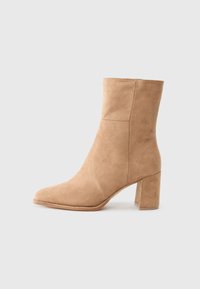 Beige suede ankle boot with a pointed toe, block heel, and smooth texture. Features minimal stitching for a clean design.