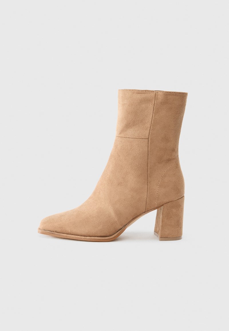 Beige suede ankle boot with a pointed toe, block heel, and smooth texture. Features minimal stitching for a clean design.
