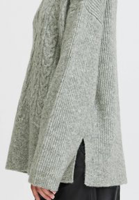Hellgrüner Strickpullover mit strukturiertem Zopfmuster, gerippten Ärmeln und seitlichen Schlitzen. Aus weichem, gemütlichem Material hergestellt.