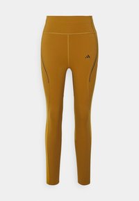 Leggings de tiro alto y ajustados en color amarillo mostaza con detalles en negro. Fabricados con material elástico y cuentan con costuras laterales para un aspecto aerodinámico.