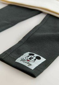 Hallatud hallid puuvillased püksid, millel on ribakujuline tekstuur, koos valge sildiga, millel on must Mickey Mouse'i graafika ja nimi "Mickey" kalligraafias.