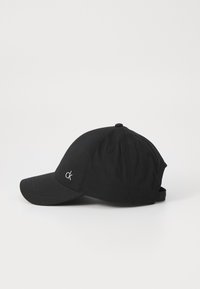 Svart baseball caps laget av stoff, med en buet skygge, justerbar stropp, og en liten brodert logo på fronten.