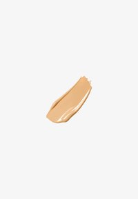 Beige flytende foundation-svamp med en jevn, kremaktig tekstur; svakt glanset finish og avsmalnet kant, satt mot en hvit bakgrunn.