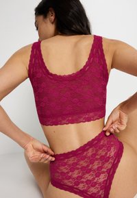 Bordeaux kanten bralette met een bloemenpatroon en gegolfde randen, gecombineerd met bijpassende hoge kanten panties, die een doorschijnende textuur laten zien.