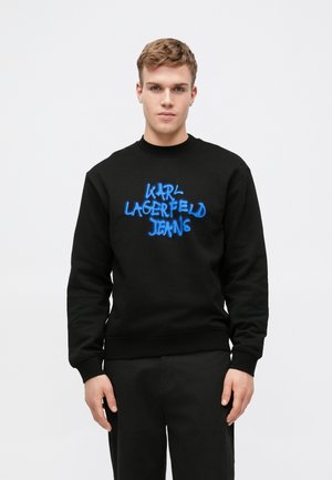 Crna dukserica dugih rukava s rebrastim manžetama. Na prednjoj strani se ističe istaknuti plavi sprejem oslikan logo "Karl Lagerfeld Jeans".