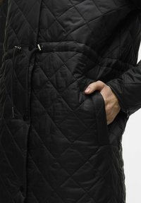 Zwarte gewatteerde jas met een ruitpatroon, verstelbare trekkoord taille en zijzakken. Glad, glanzend materiaal met buttonsluiting.